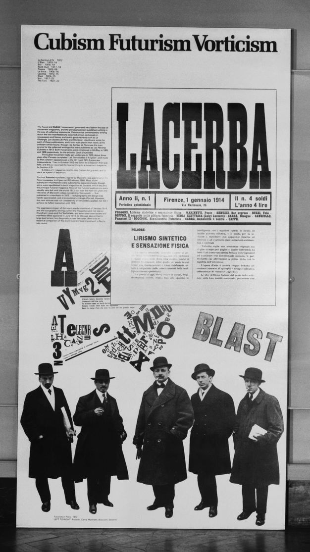 Installation. Black and white photograph of a panel titled “Cubism Futurism Vorticism”. Periodical covers and mastheads overlap over a picture of five men wearing brimmed hats and shin-length dark trench coats.